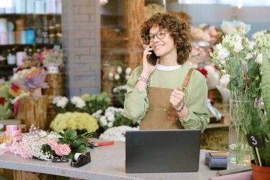 Kafkas çiçekçisinin dükkânda çalışırken akıllı telefondan sırayla konuştuğu orta boy yakın çekim.