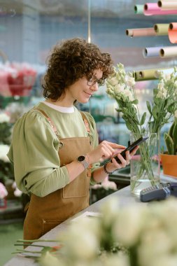 Kadife önlüklü yetenekli çiçekçinin dükkânda çalışırken ağları kontrol ederken çekilmiş dikey yakın plan fotoğrafı.