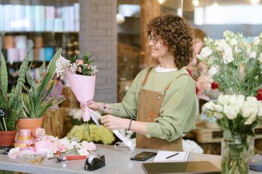 Gülümseyen çiçekçi elinde zarif bir buket ve saten kurdeleli bir fiyonk tutuyor.