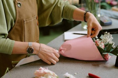 Pastel pembe ambalaj kağıdını ayarlayan tanınmayan kadın ellerinin orta derecede yakın çekimi.