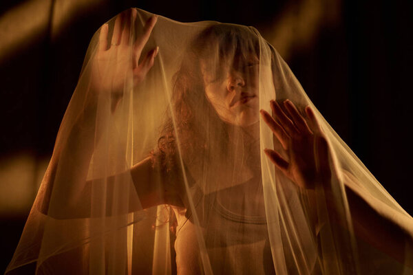 Низкоугольный снимок кудрявой молодой женщины с закрытыми глазами, прячущейся под вуалем