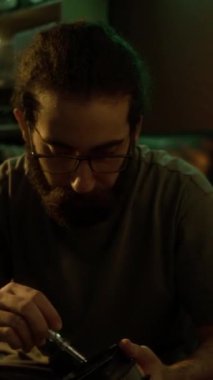 Gülümseyen sakallı adamın dikey portresi güneş ışığında yeşil bir parıltıyla CPU soğutucusunu tamir ederken, güneşli odada yerde otururken.