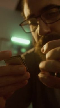 CPU çipini inceleyen sakallı adamın dikey yakın çekimi, güneş ışığında yeşil ışıklı odada otururken.