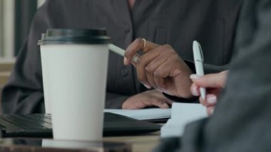 Kahve molası sırasında elinde kalemle kafeteryada dizüstü bilgisayarla oturan tanınmayan iş arkadaşlarının yakın çekimleri.