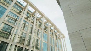 Alçak açı, iş elbiseli genç bir kadının elinde hazır kahve fincanı güneşli bir günde modern binalarla işe yürüyerek gitmesi.