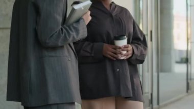 Resmi kıyafetli tanınmayan iki kadın modern binanın dışında el sıkışıyor ve uzaklaşıyorlar.