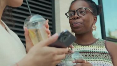 Güneşli yaz gününde, iki gülümseyen bayan arkadaşın dışarıda içkilerini yudumlarken yakın plan çekimleri.