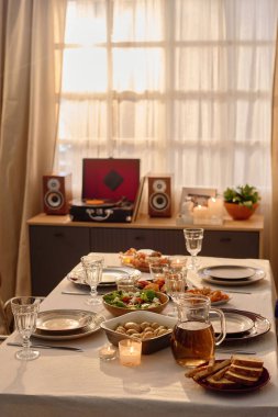 Vertical shot of table covered with white tablecloth and served with homemade food, table located near wooden dresser with speakers and retro vinyl record clipart