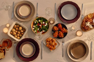 Top down shot of table fully served with clean and polished cutlery and tableware, homemade food in center of table decorated with white cotton tablecloth and lit wax candles clipart