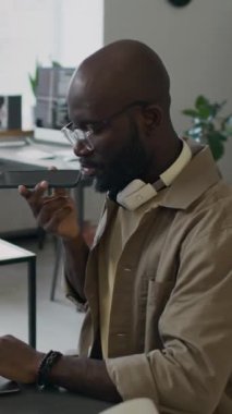 İş yerinde kodlama yaparken iş ortağıyla telefonda konuşan siyahi erkek geliştiricinin dikey görünümü