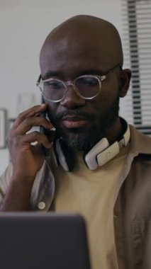 Boynunda gözlük ve kulaklıkla binlerce yıllık Afro-Amerikan erkek yazılım geliştiricisinin müşteriyle telefon görüşmesi yaparken dikey görüntüsü