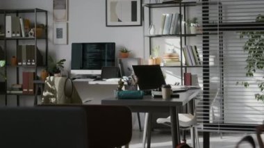 Hiç kimse masasında bilgisayar olan modern bilişim şirketinin ofisine bakmıyor, iki rafta dosya klasörleri ve raflarda kitaplar olan iki raf, duvarda soyut tablolar