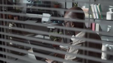 Afrika kökenli, kel, gözlüklü, güç adaptörü kullanan ve iş gününde laptopta kod yazan bir programcı.
