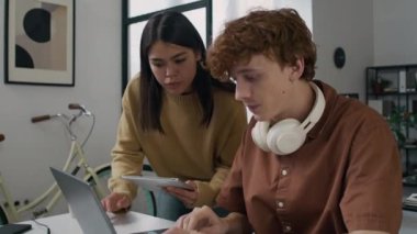 İki farklı genç bilgisayar programcısı şirket ofisindeki laptop ekranına bakarak yazılım geliştirmeyi tartışıyor.