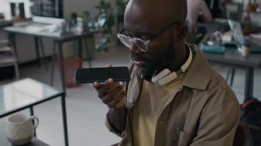 İş yerinde bilgisayarında kodlama yaparken, iş arkadaşıyla telefonda konuşan siyah erkek web geliştiricisini aşağı eğ