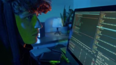 Kafkasyalı kıvırcık saçlı adamın bilgisayar sistemini hacklediği ve karanlık ofise virüs bulaşmış yazılım yüklediği yakın plan görüntüsü.