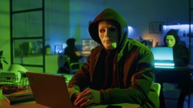 Gece ofiste dizüstü bilgisayar kullanırken kameraya ciddi bir şekilde poz veren bilgisayar suçlusu erkek portresi