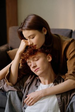 Kafkasyalı bir kadının kanepede oturup yerde oturan erkek arkadaşını okşamasının dikey görüntüsü.