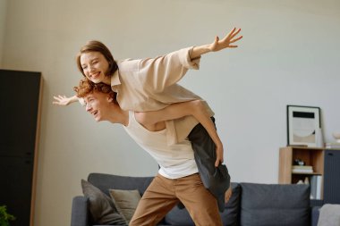 Gülümseyen adamın kollarını kanat gibi düzleştirirken kız arkadaşının sırtına bindiği düşük açılı çekim.