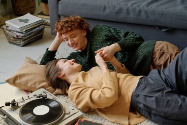 Arka planda retro vinil kaydedici çalarken genç beyaz bir çiftin sohbet ve kahkahalar attığı yüksek açılı bir çekim.