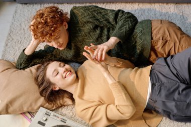 Genç, mutlu, beyaz bir çiftin yumuşak halıda dinlenip el ele tutuşup onları okşadığı yüksek açılı bir çekim.