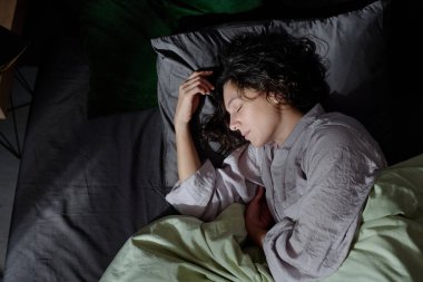 Pamuklu pijama giymiş kıvırcık saçlı esmer kadının pamuklu keten kumaşla yeni yatakta uyumasının keyfini çıkarırken.