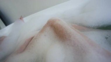 Genç bir kadının kalçasına, dizine ve bacağına dokunduğu ve hafta sonları sıcak köpük banyosunun keyfini çıkardığı yakın plan görüntüsü.