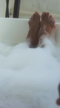 Baloncuklarla dolu küvette uzanan ve spa ameliyatının keyfini çıkaran tanınmayan bir adamın dikey görüntüsü.