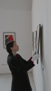 Asyalı kadının soyut tabloları sıraya dizip sanat galerisindeki sergiye hazırlandığı dikey bir fotoğraf.