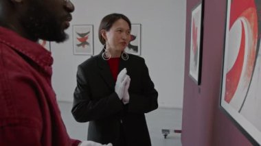 Asyalı kadın ve Afro-Amerikan erkek, şık günlük kıyafetler içinde minimalist sanat galerisinin duvarındaki soyut resimden bahsediyorlar.