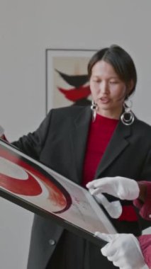 Asyalı sanat küratörü ve tanınmayan asistanının sanat galerisinde resim sergisini dikey çekimleri.