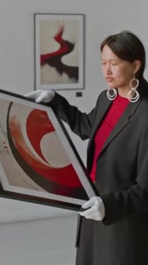 Resmi sanat galerisinde duvara asmadan önce, Asyalı bir kadının sıradan bir takım elbiseyle resme baktığı dikey bir fotoğraf.