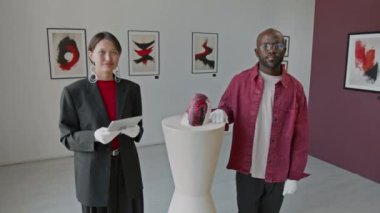 Asyalı ve Afrikalı Amerikalı sanat galericilerinin portresi, kamera önünde poz vermek, minimalist sanat galerisinin temel taşının yanında durmak.
