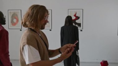 Broşür okuyan adam, diğer iki kişi minimalist sanat galerisindeki sergi sırasında duvarlarda soyut resimler görürken,