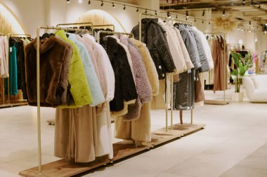 Kısa ve uzun renkli kürk mantoları, şık kadın kıyafetlerinden oluşan butikte askılara asılıydı.