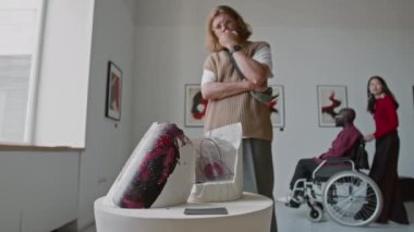 Sakallı adam düşünceli bir şekilde soyut heykeli incelerken, tekerlekli sandalyedeki siyah adam ve Asyalı kadın minimalist sanat galerisindeki duvarlara hayran kalıyorlar.