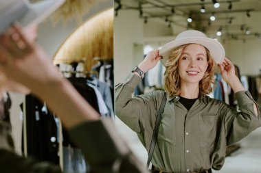 Beyaz plaj şapkası takan ve aynaya bakan bir kadının görüntüsü.