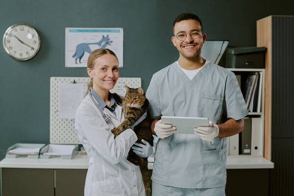 Портрет ветеринаров, стоящих в клинике, держащих кошку и улыбающихся в камеру, проявляющих заботу и профессионализм в уходе за животными