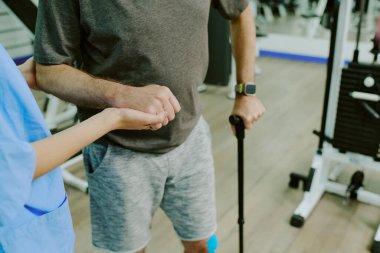 Ciddi bir diz sakatlığından sonra birlikte yürümeye çalışırken doktorun hastaların elini tutarken yüksek açılı görüntüsü.