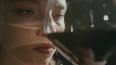 Karamsar, beyaz bir kızın şarap dolu bardağa bakıp yüzüne yakın tutuşu.