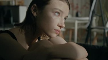 Kanepede oturup dizlerini göğsüne dayayıp rahatsız edici düşünceler besleyen sinirli genç bir kadının yakın çekimi.