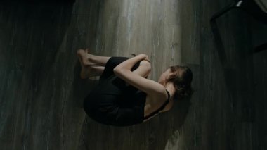 Siyah kimya giymiş, yerde yatıp dizlerine sarılırken panik atak geçiren zavallı bir kadının yüksek açılı görüntüsü.