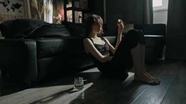 Siyah gecelik giymiş genç bir kadın oturma odasının camının yanındaki kanepede sırtüstü yatarken şişeden açık ellere bazı haplar döker.
