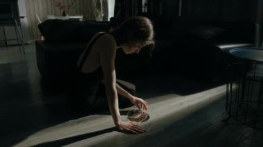 Siyah gecelik giyen paranoyak genç bir kadın kırık yuvarlak ayna parçasını alıp oturma odasında yerde otururken şüpheli bir şekilde pencereye bakıyor.