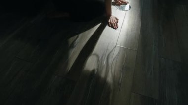 Oturma odasının zeminindeki loş ışıkta kırık aynaya bakan genç kadının görüntüsünü kaldır.