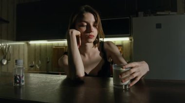 Duygusal çöküntüye uğramış bir kız üzerinde haplarla mutfak masasında otururken kasıtlı olarak bardaktan süt döküyor ve su birikintisine dokunuyor.