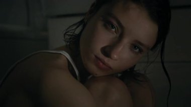 Kameraya poz veren kırık kalpli kızın yakın plan portresi. Banyo loş ışıklarıyla göğsüne diz çökerken.