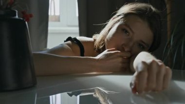 Kamera önünde poz veren Z jenerasyonundan bir kızın portresi. Sabahın erken saatlerinde mutfak masasında çenesini onların üzerinde dinlendirirken diğer tarafa bakıyor ve kollarını kavuşturuyor.