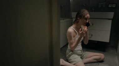 Beyaz kolsuz bluz giyen, açık renkli şort giyen, banyoda telefonda bağıran ve ağlayan fevri bir beyaz kadın.