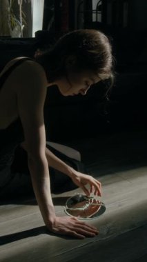 Endişeli genç bir kadının, oturma odasının zemininde otururken kırık ayna parçasına bakması dikey bir bakış açısı.